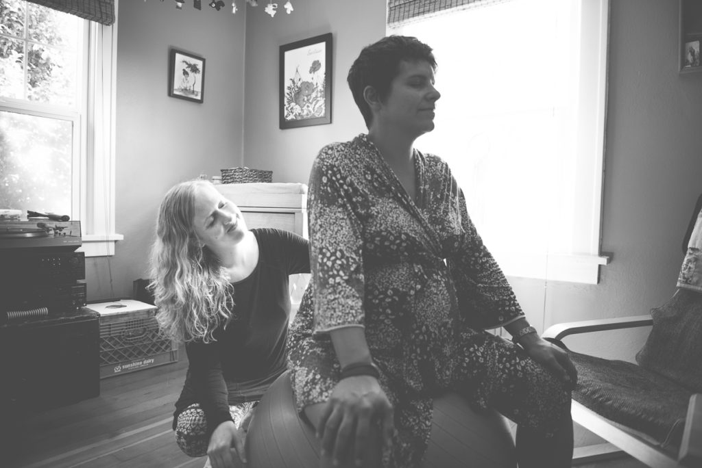 Close up Allie Machen performing a doula service by rubbing the back of her pregnant patient who is sitting on an exercise ball.