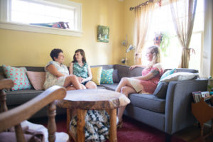 Allie Machen sitting in the living room with her pregnant client and her wife on the couch.