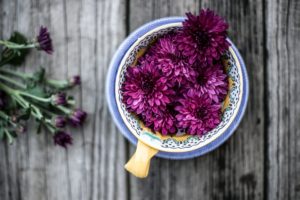 Purple dahlia flowers heads in a bowl on a rustic wooden table.